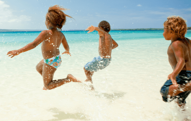 A group of children on a whote sandy beach running into the water