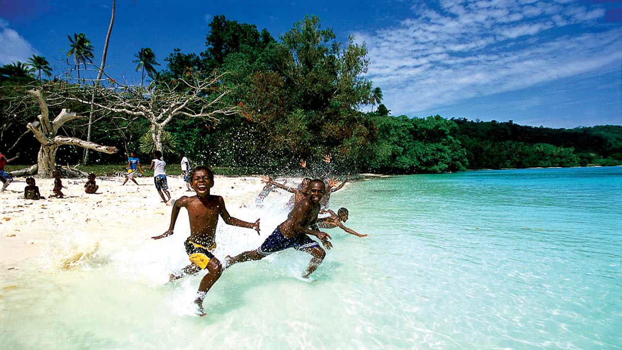 Children running into the water on a white sandy beach in Port Vila, Efate
